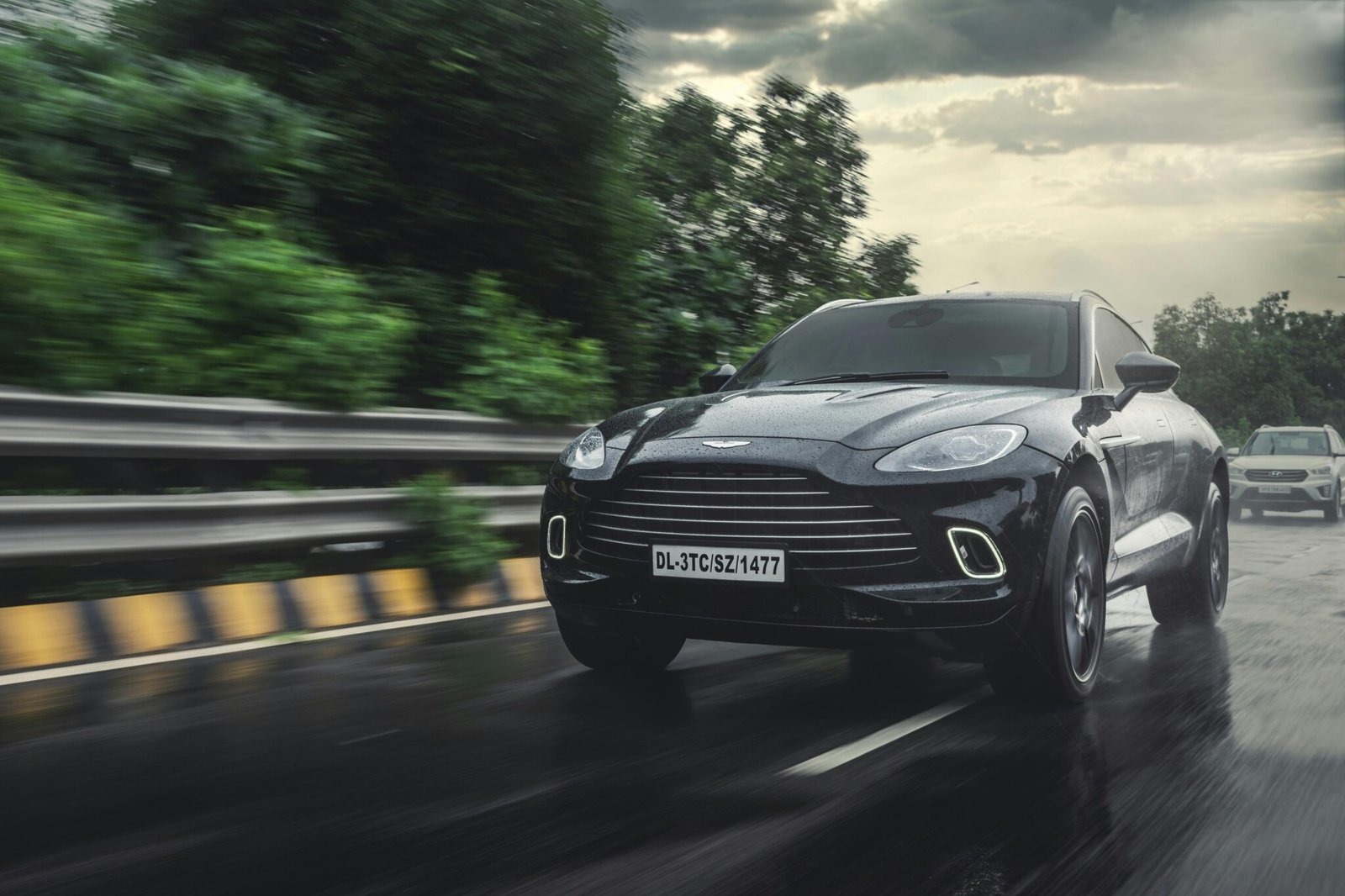 Black SUV driving fast on a wet highway under cloudy skies, showcasing speed and elegance.