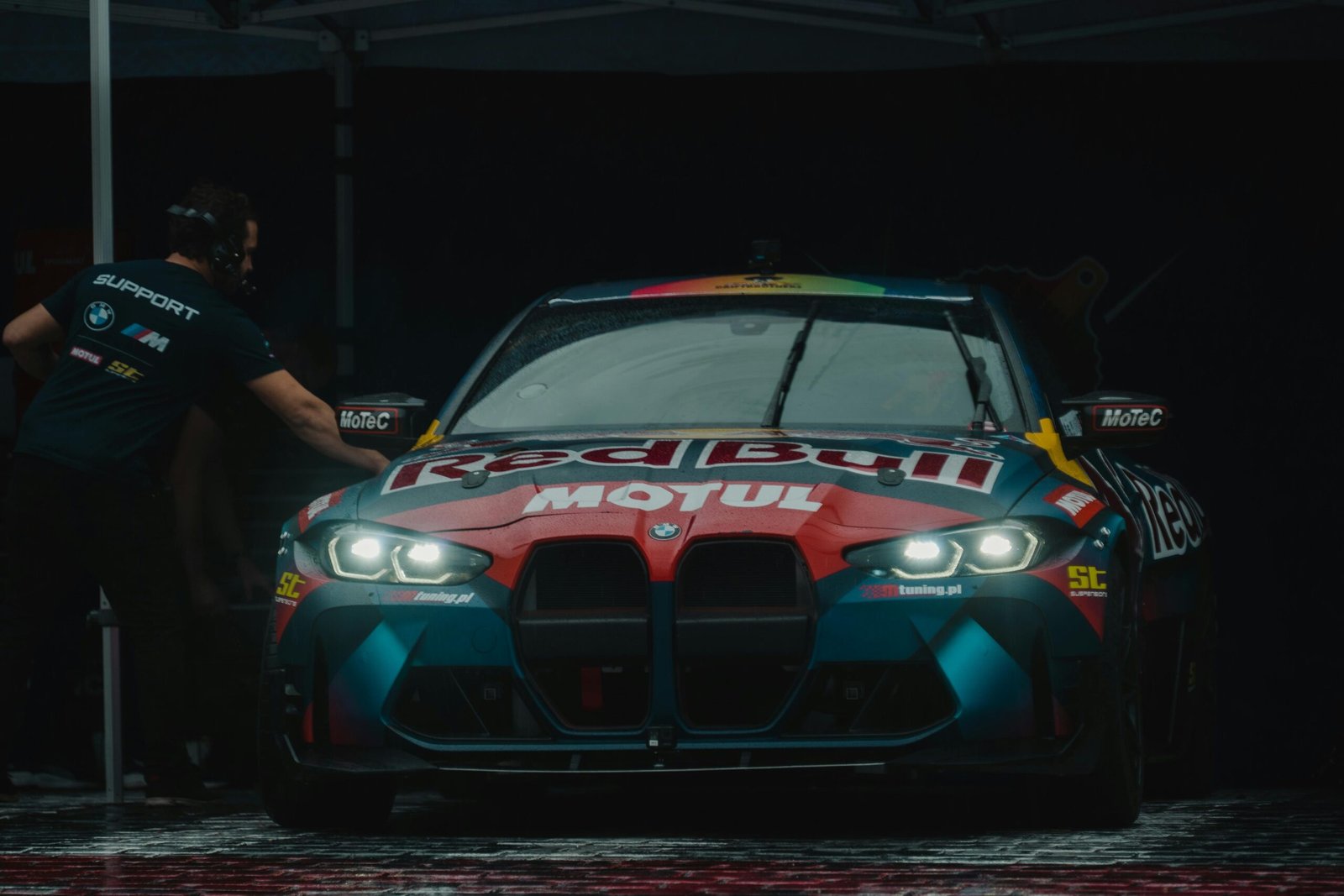 Front view of a BMW M4 race car featuring Red Bull Motul branding under dim lighting.
